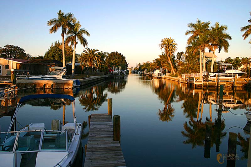 Calm waters of a canal reflecting palms and boats.