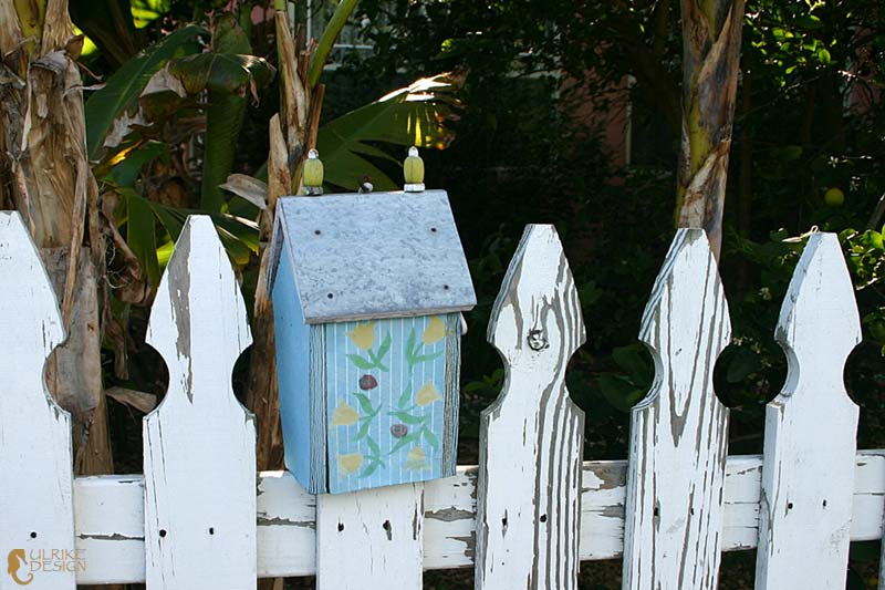 A little bird house perched on a weathered fence.